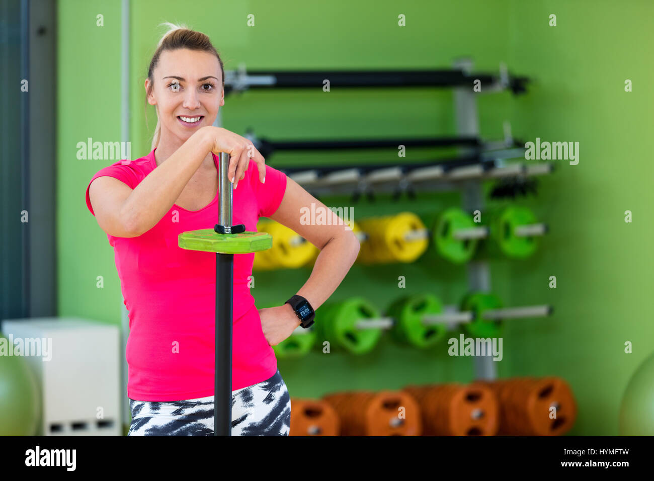 Colocar a la mujer en un gimnasio mirando a la cámara, descansando después del ejercicio con barbell. Foto de stock