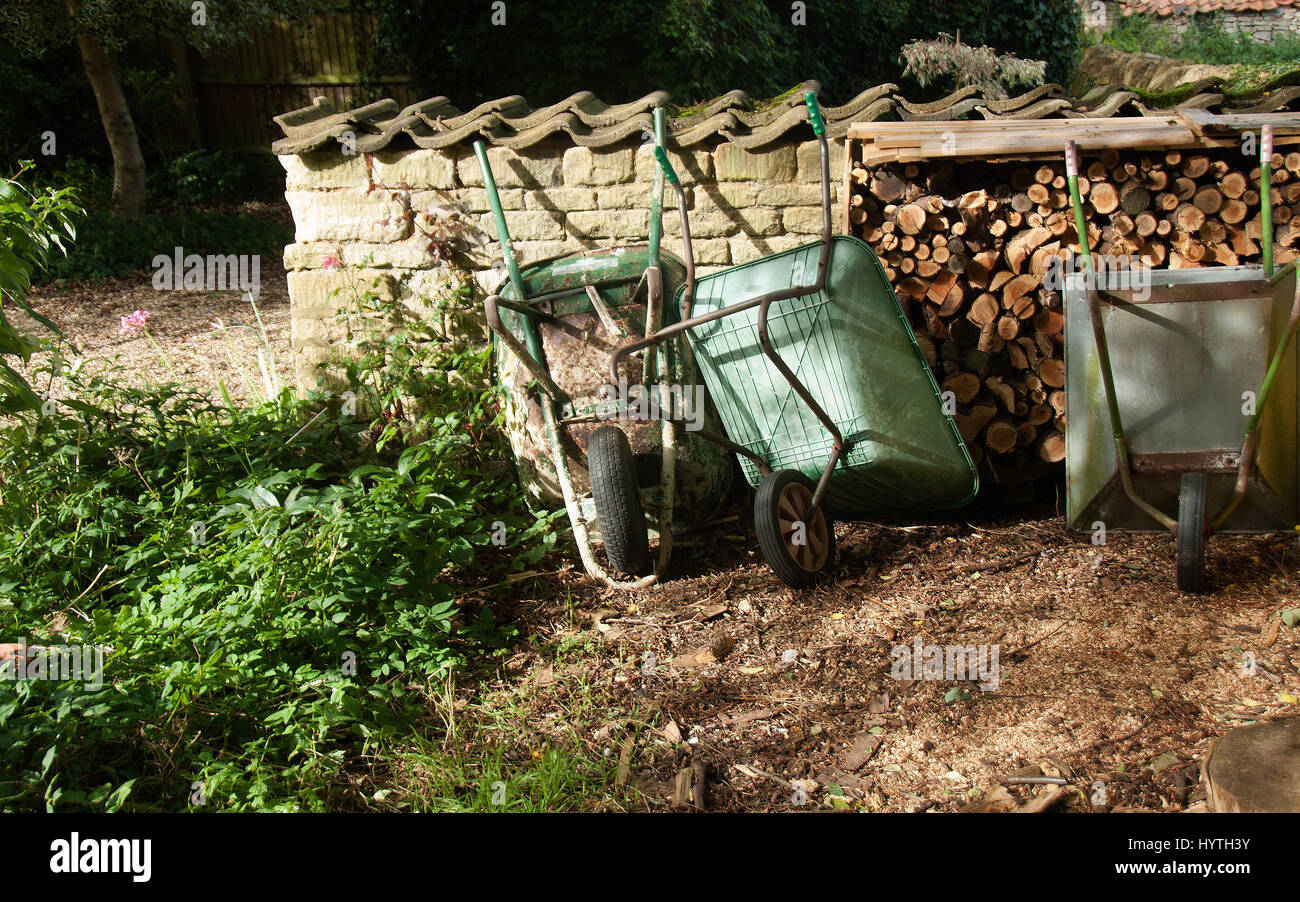 Tres carretillas antigua rústica junto al montón de madera en un jardín rural Foto de stock