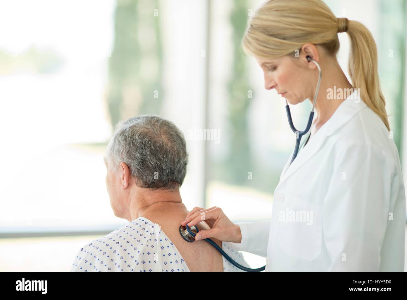 Doctora con estetoscopio en paciente masculino. Foto de stock
