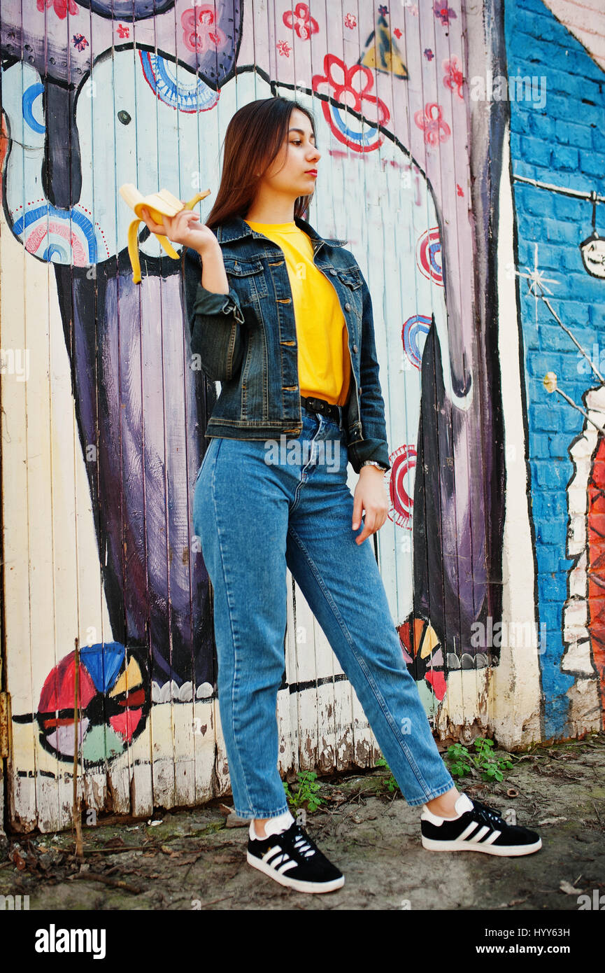 Hermosa chica adolescente comer bananas, vestir de amarillo t-shirt, jeans  cerca de graffiti wall Fotografía de stock - Alamy