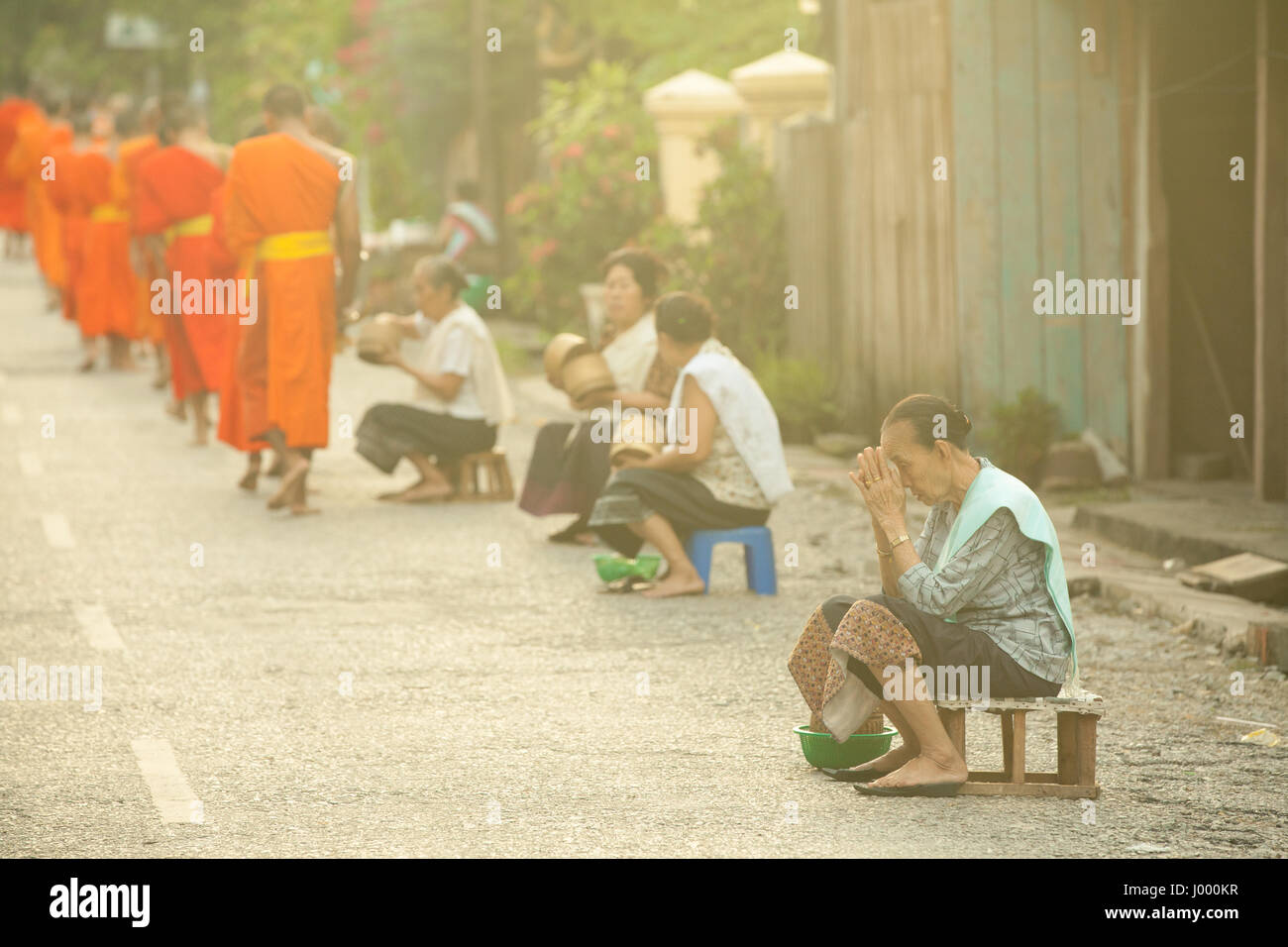 La República Democrática Popular Lao, Laos, Luang Prabang - 20 DE JUNIO: Mujer ora después de dar limosna a los monjes budistas en la calle, en Luang Prabang. Foto de stock