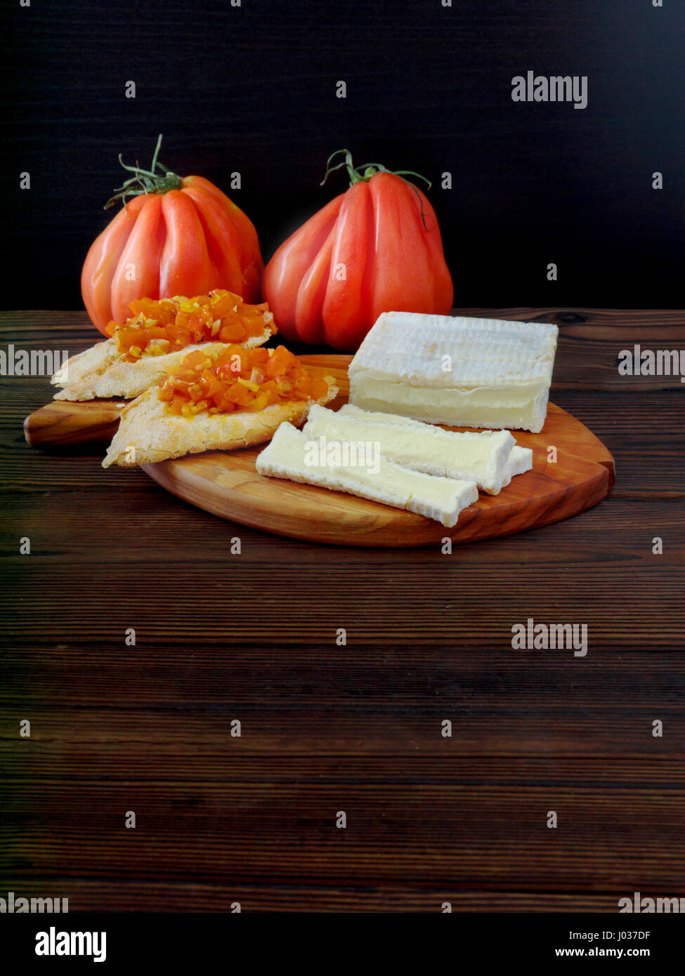 Queso con forma de ladrillo con moho blanco, tomates y las tostadas Foto de stock