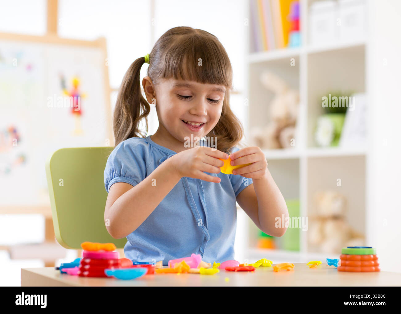 Chico Chica está jugando con plastilina mientras está sentado en la mesa Foto de stock