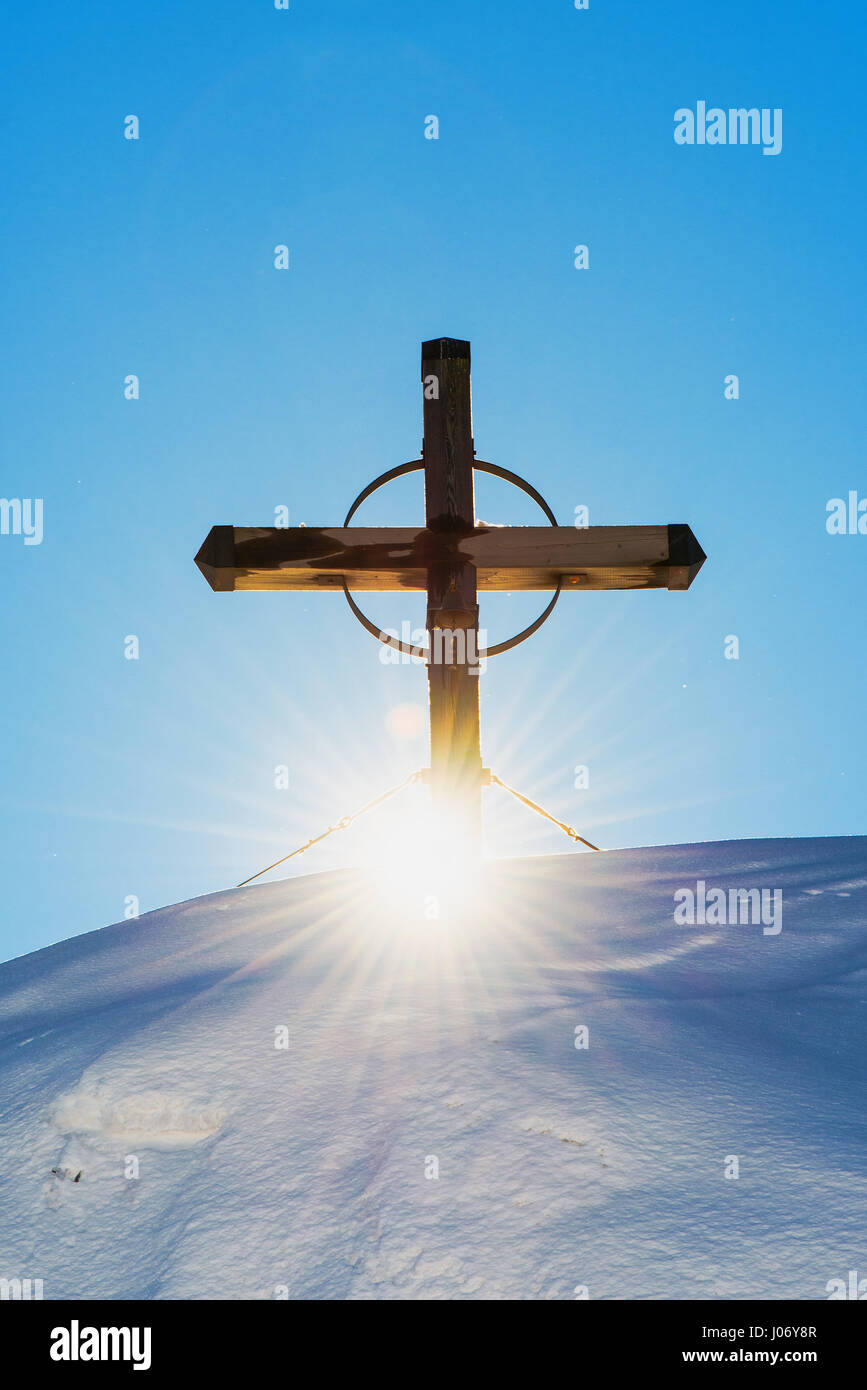 El cristianismo religioso cruz de montañas cubiertas de nieve, la luz solar atravesando Foto de stock