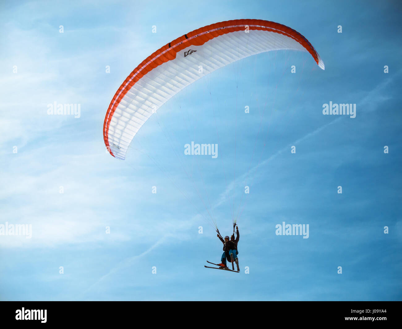Dos practica parapente con esquíes volando contra el cielo azul en el clima soleado. Foto de stock