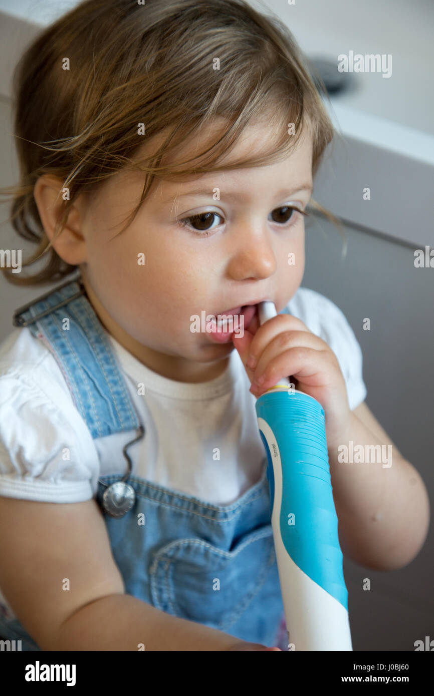 Niña Niño cepillarse los dientes con un cepillo de dientes infantil, y la  celebración de un adulto cepillo eléctrico en su otra mano. Ella es de 16  meses de edad Fotografía de