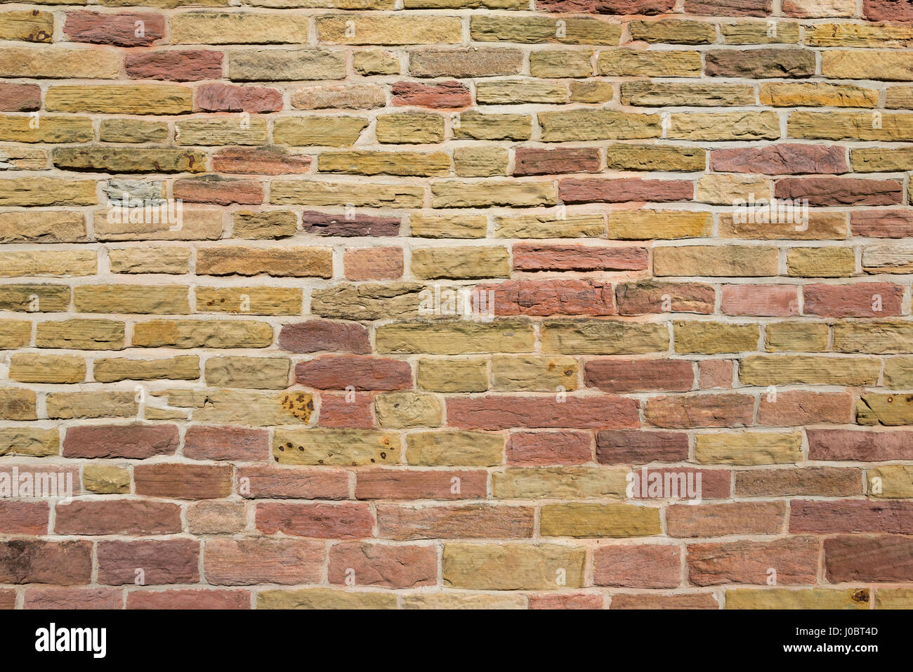 Muro de piedra de colores cálidos. Patrón abstracto de albañilería antigua en una pequeña iglesia en Chadkirk, Stockport, Inglaterra. Foto de stock