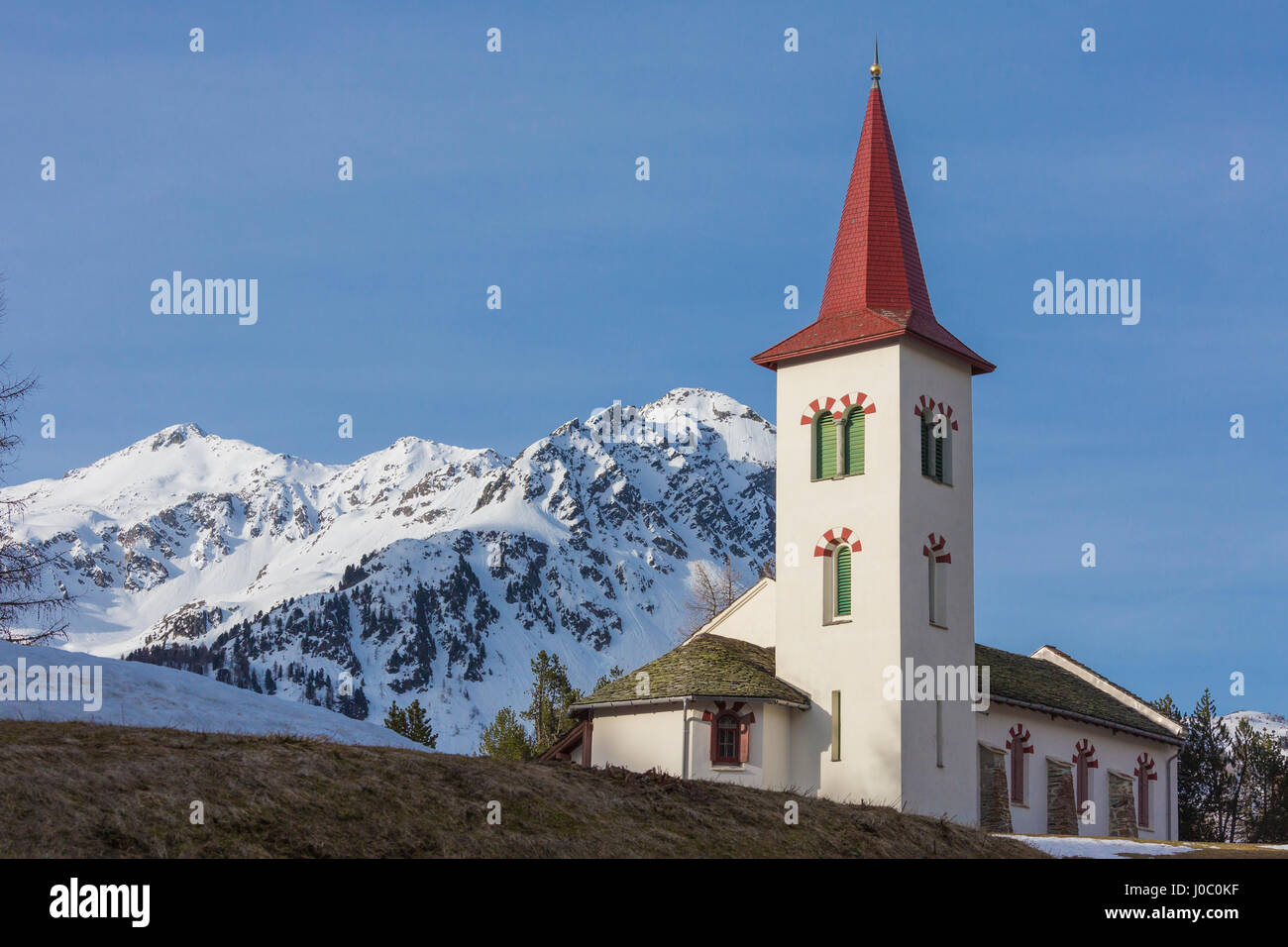 La iglesia alpina blanca enmarcada por picos nevados, Maloja, Bregaglia Valle, Cantón de Graubunden, Engadin, Suiza Foto de stock