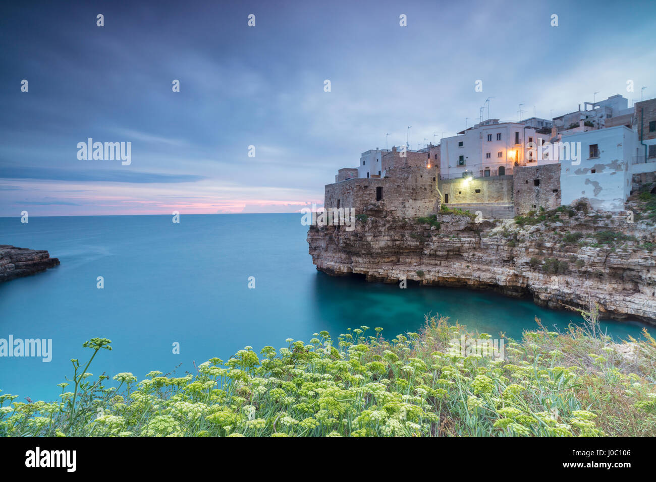 Mar turquesa al amanecer enmarcada por el casco antiguo de la ciudad, encaramado en las rocas, en Polignano a Mare, Provincia de Bari, Puglia, Italia Foto de stock