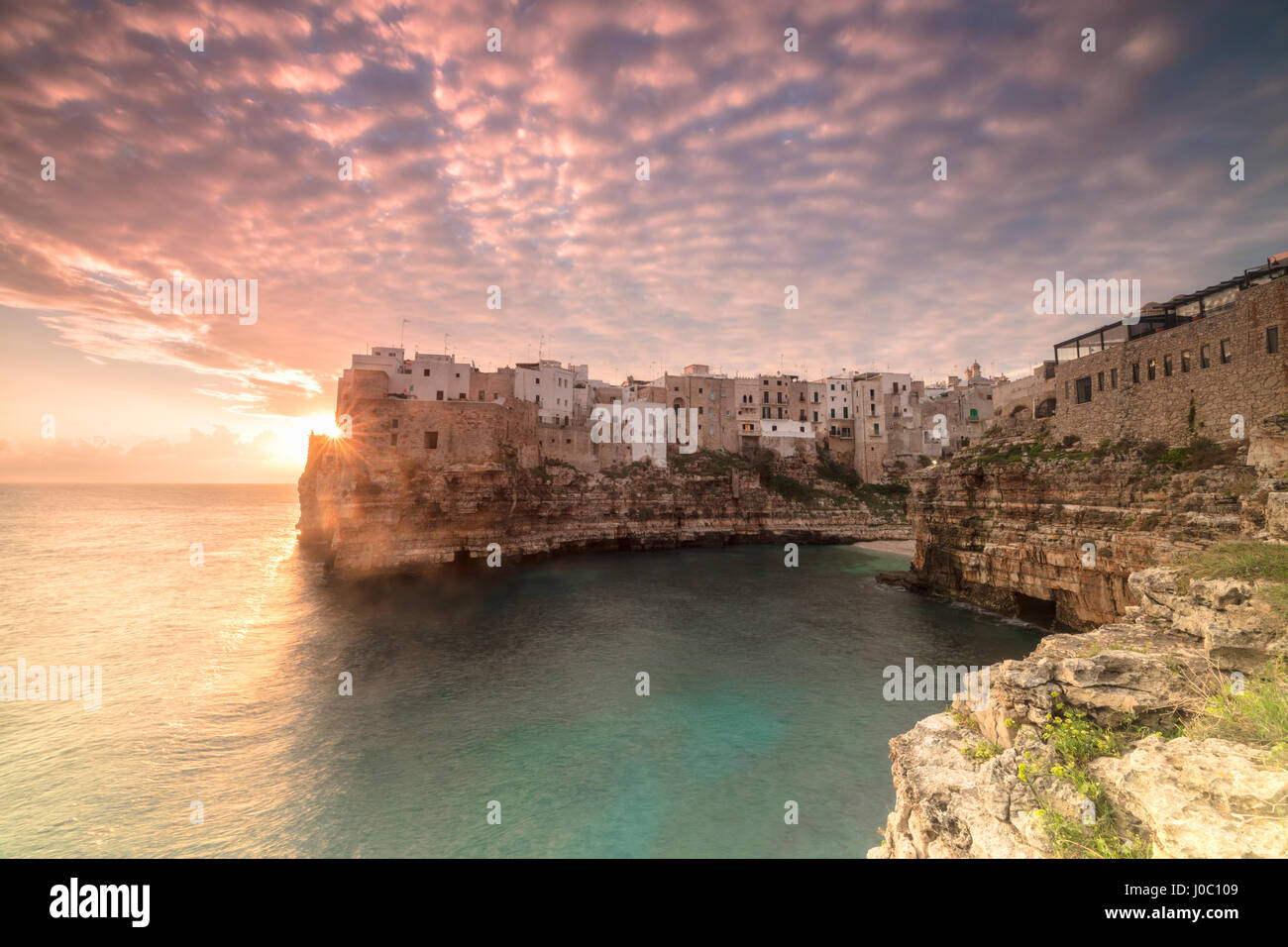 Rosa del amanecer sobre el mar turquesa enmarcado por la vieja ciudad encaramada sobre las rocas, en Polignano a Mare, Provincia de Bari, Puglia, Italia Foto de stock