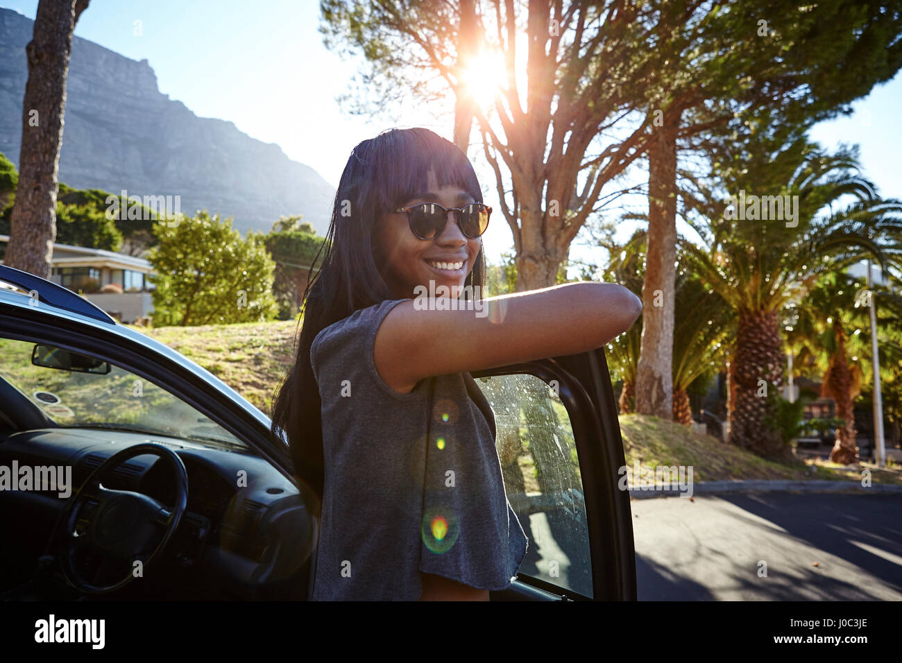 Retrato de mujer joven de pie junto al coche, apoyándose en abrir puerta del automóvil Foto de stock