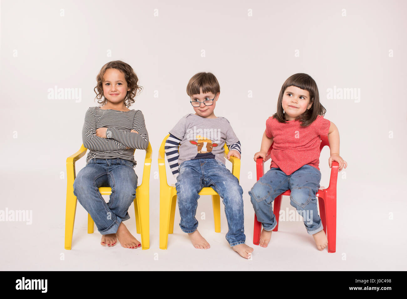 Retrato de tres niños sentados en sillas de colores, Foto de estudio Foto de stock