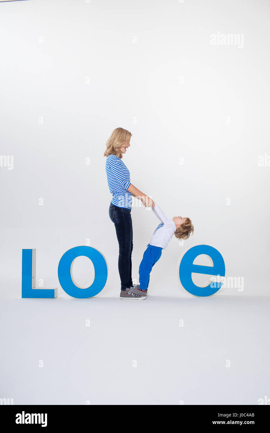 Madre e hijo cogidos de la mano, de pie entre letras tridimensionales, creando la palabra AMOR Foto de stock