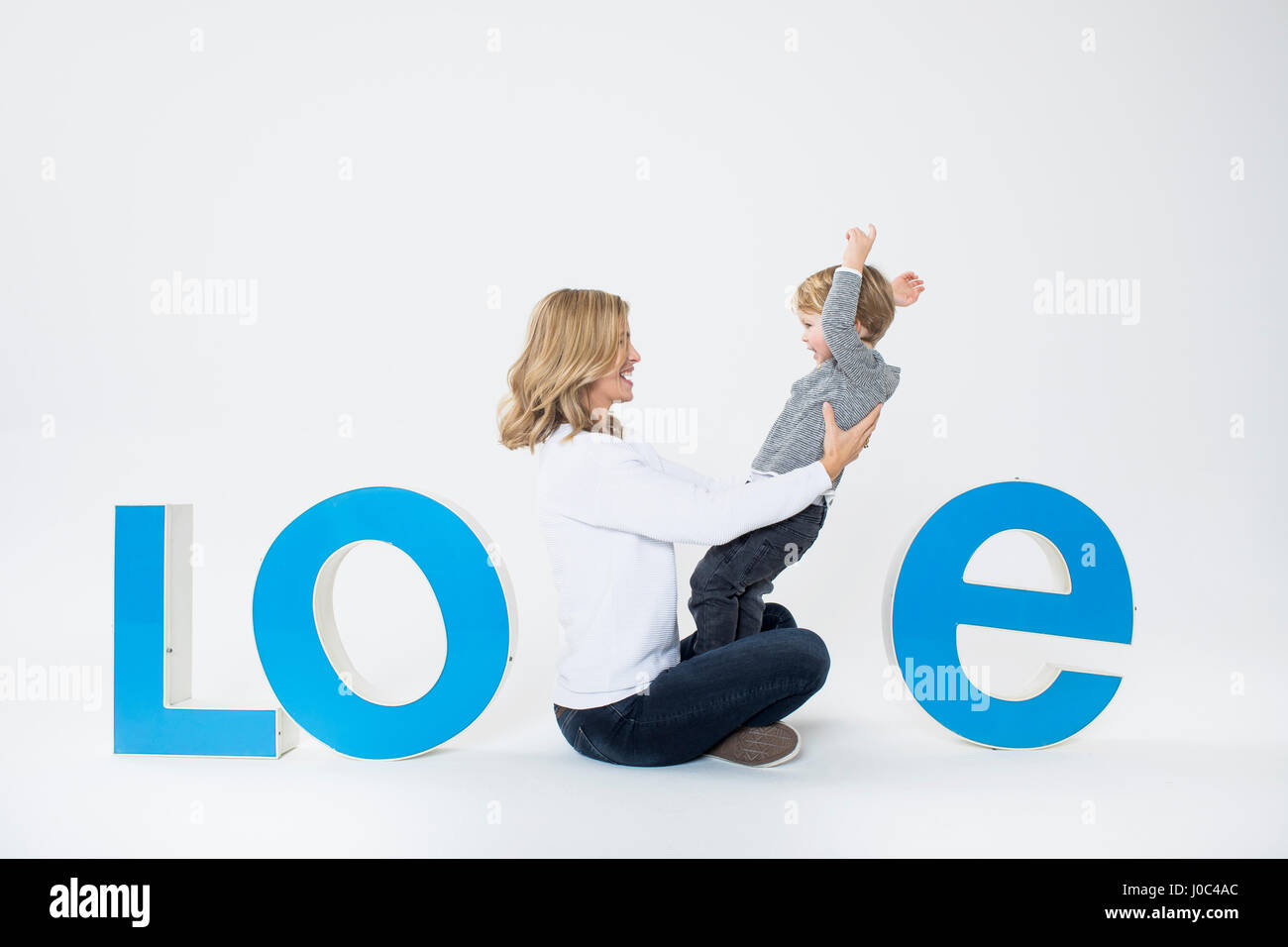 Madre e hijo sentado entre letras tridimensionales, creando la palabra AMOR Foto de stock