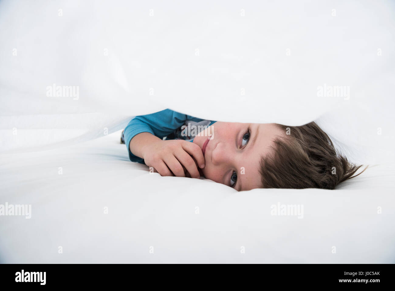 Niño acostado entre sábanas blancas Foto de stock