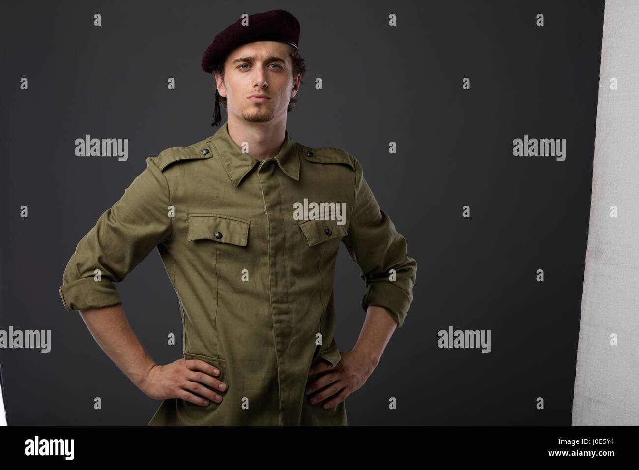 Los jóvenes militares con boina roja y verde uniforme sobre fondo gris Foto de stock