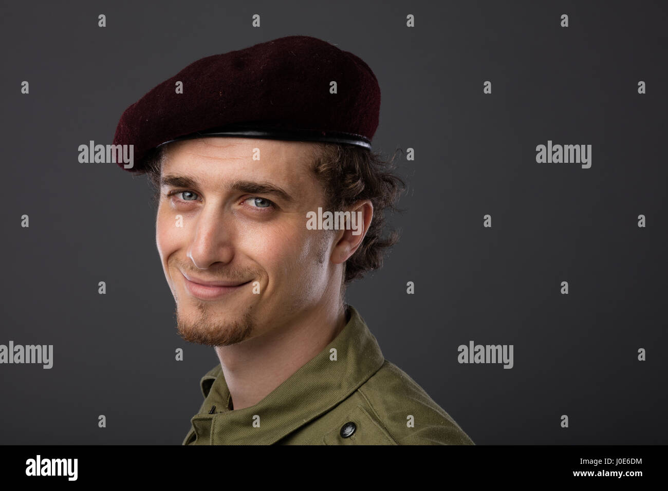 Los jóvenes militares con boina roja y verde uniforme sobre fondo gris Foto de stock