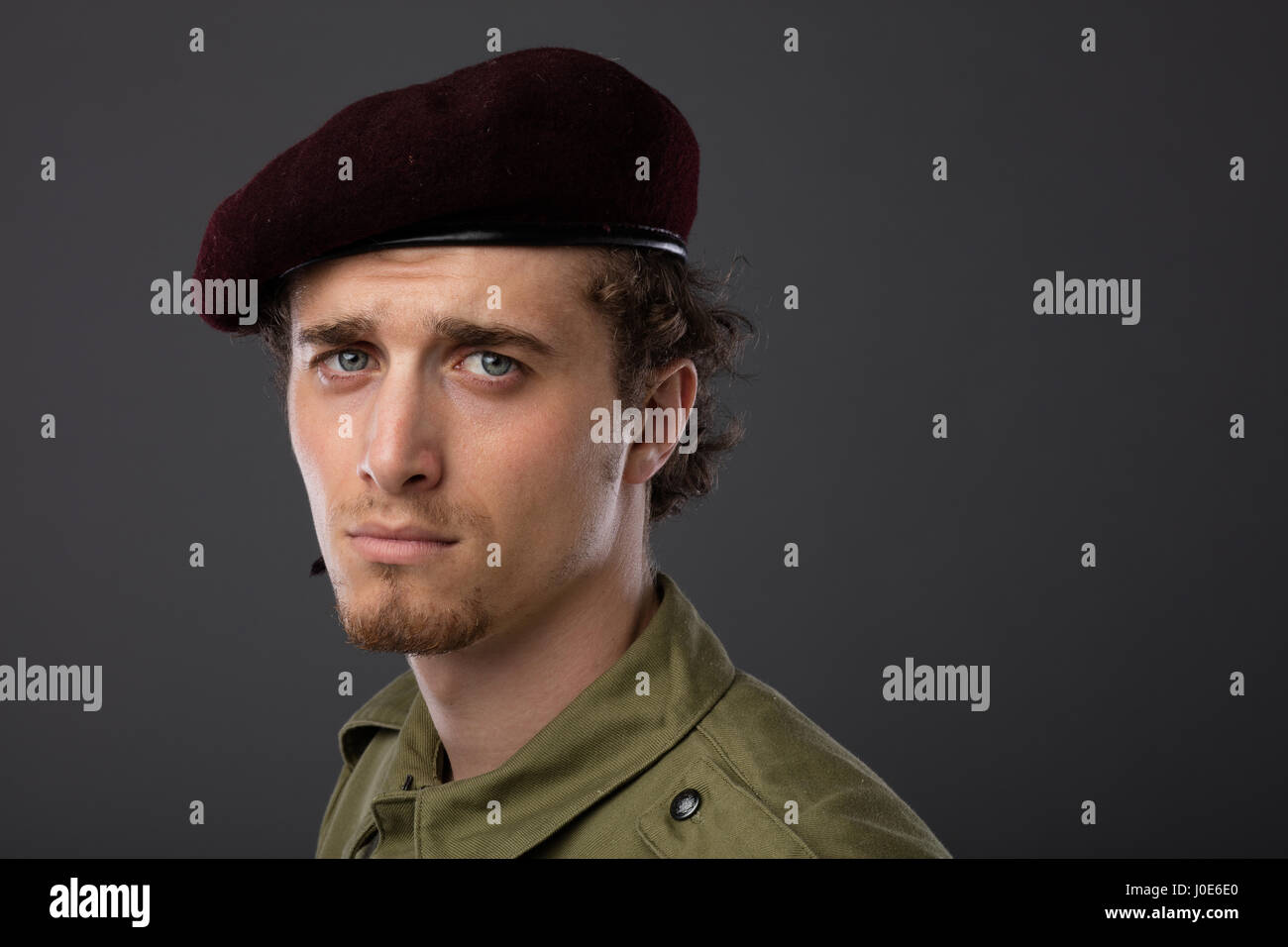 Los jóvenes militares con boina roja y verde uniforme sobre fondo gris Foto de stock