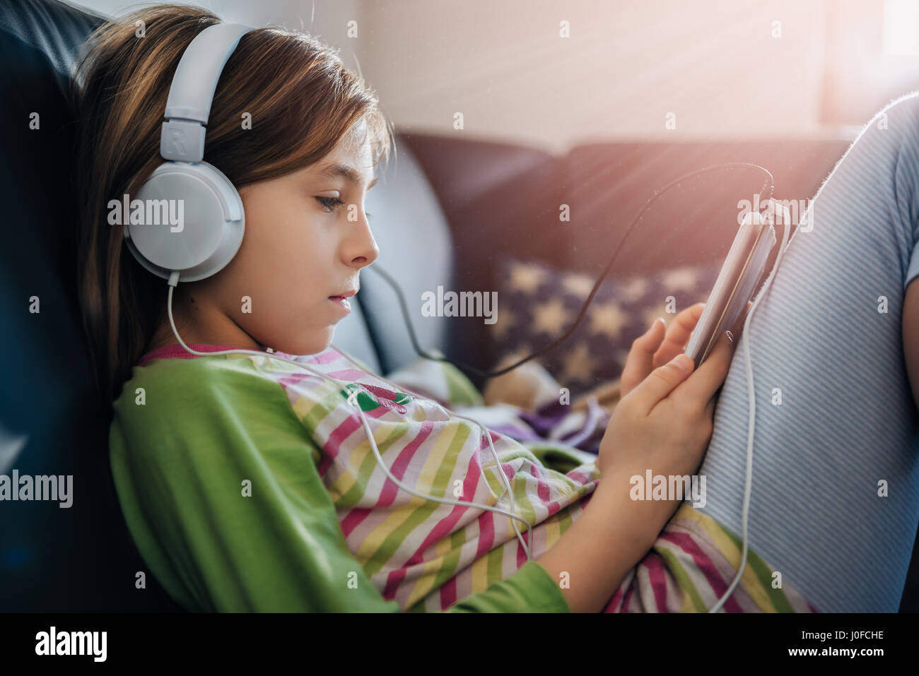 Chica sentada en un sofá negro con tablet y escuchar música Foto de stock