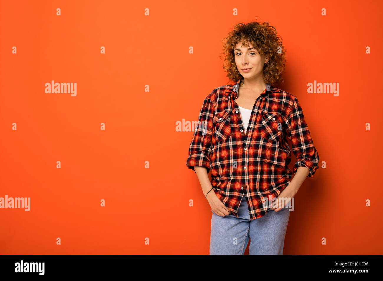 Muy mujer en una a cuadros y jeans de pie sobre un fondo de color naranja con un espacio vacío para el texto que se encuentra junto a ella Fotografía