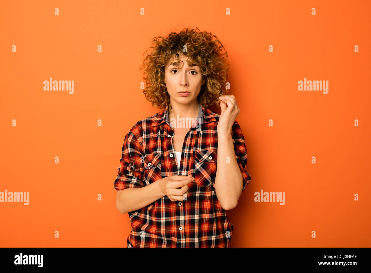 Muy rizado mujer en una camisa a cuadros y jeans de pie sobre un fondo de  color naranja con un espacio vacío para el texto que se encuentra junto a  ella Fotografía