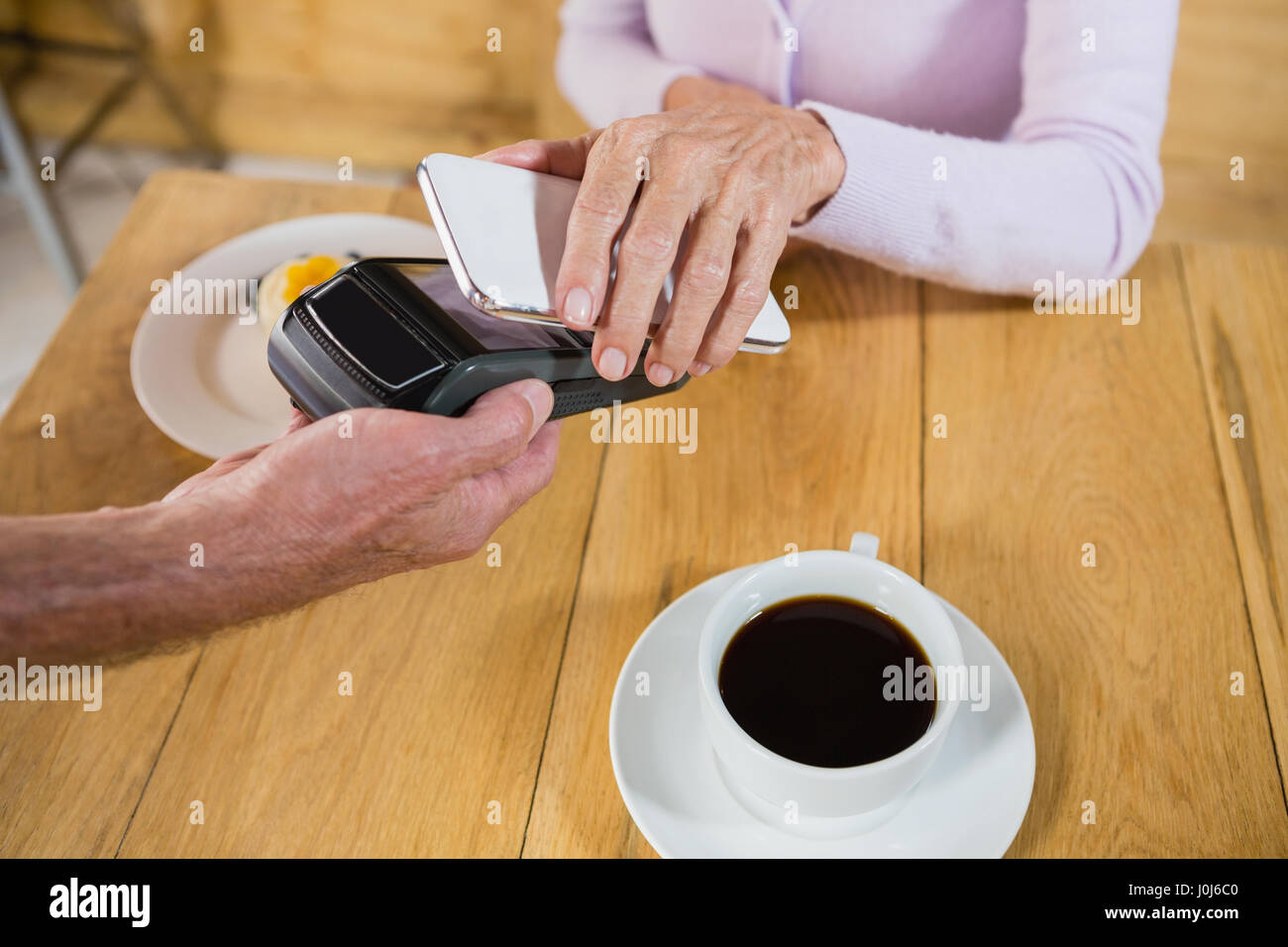 Senior mujer haciendo el pago mediante tecnología NFC en teléfonos móviles en cafÃƒÂ© Foto de stock