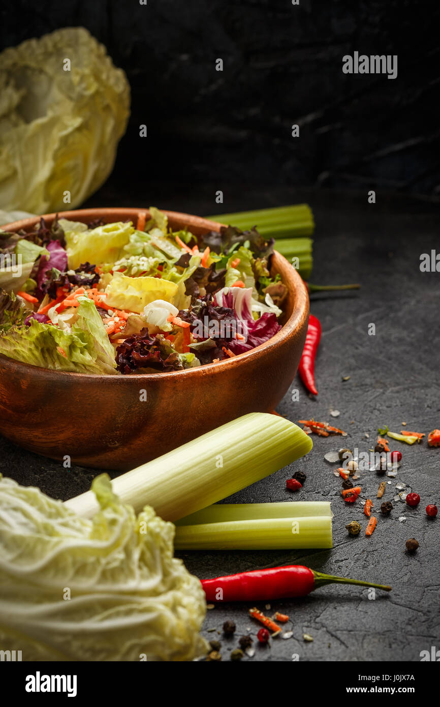Recipiente de madera con una mezcla de ensalada de congelación, Lollo Rosso, radicchio, romano y el iceberg con zanahorias sobre fondo negro Foto de stock