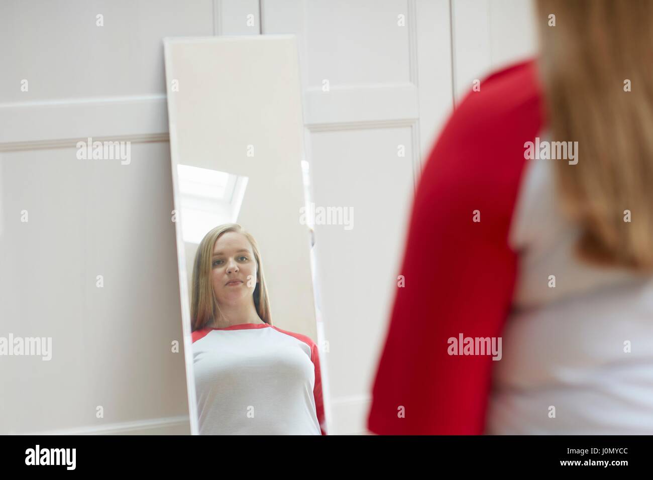 Mujer joven busca en el reflejo en el espejo. Foto de stock