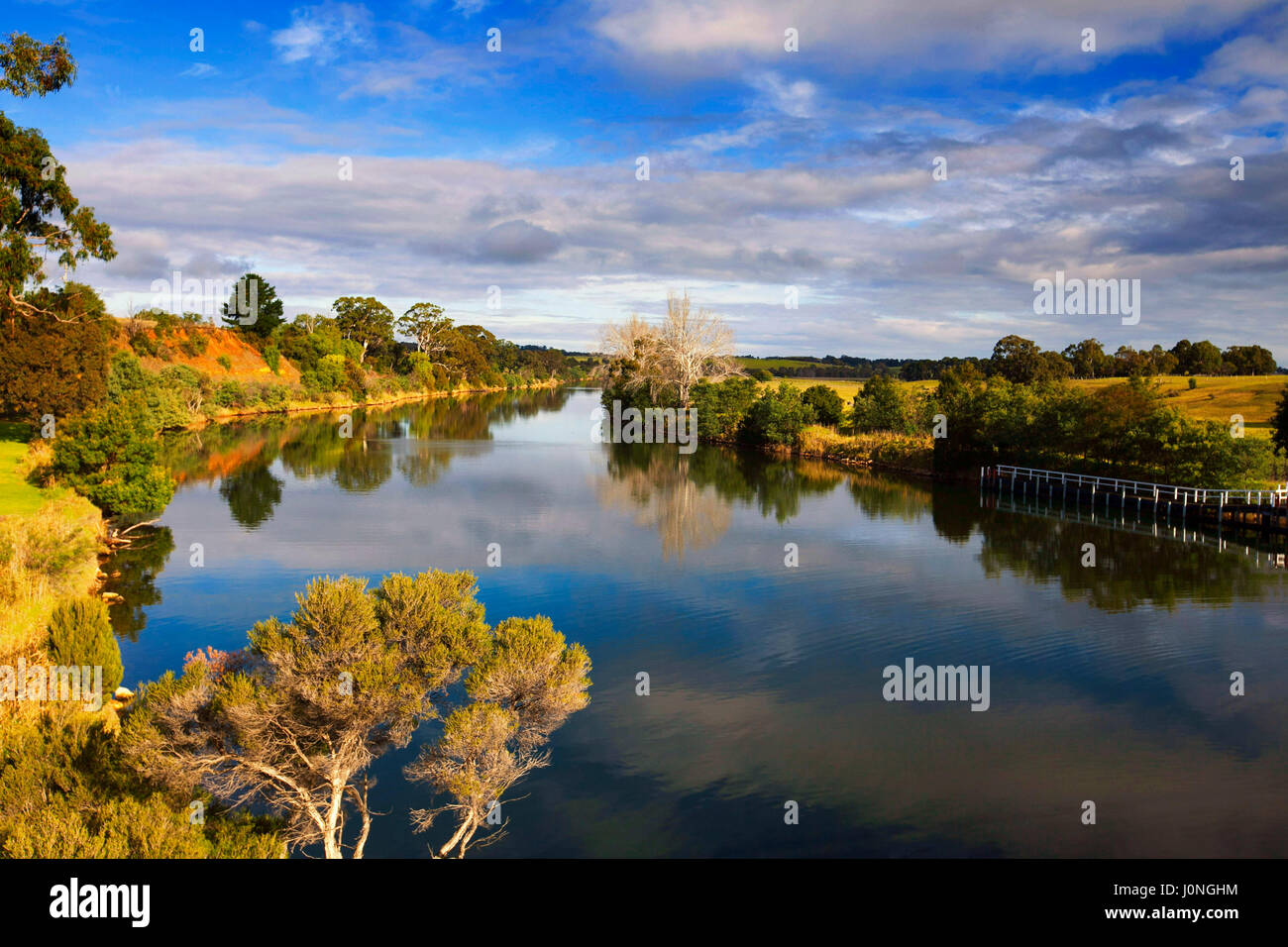 Impresionante paisaje de Australia con el cielo azul y las nubes se reflejan en la superficie del espejo del río Murray atenazada por tierras de cultivo cerca de alcanzar Swan, Victoria Foto de stock