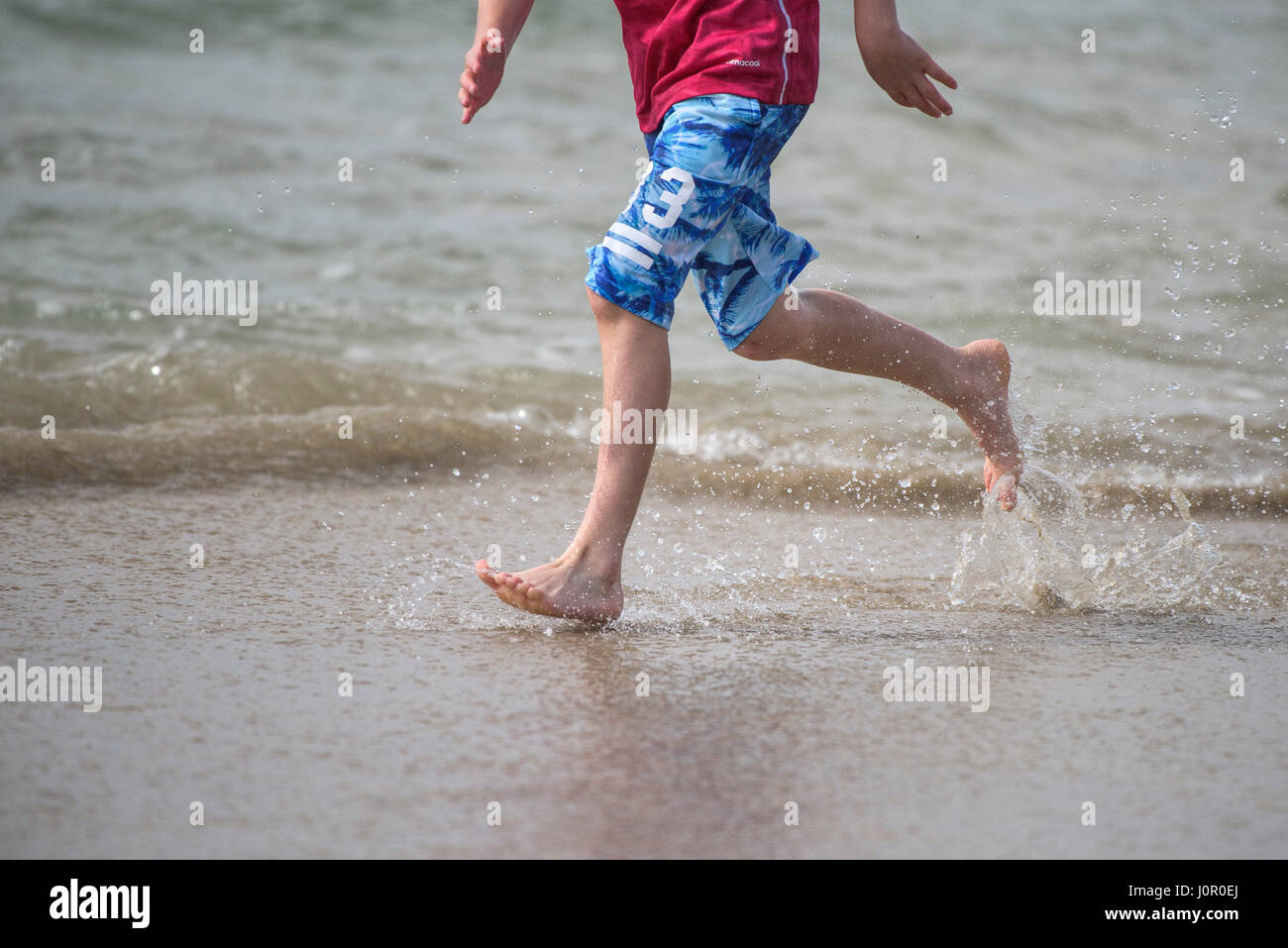 Fistral Newquay persona corriendo a lo largo de la costa Splash Runner Spray Agua Barefoot Energía energética Turismo costero vacaciones en la playa Foto de stock