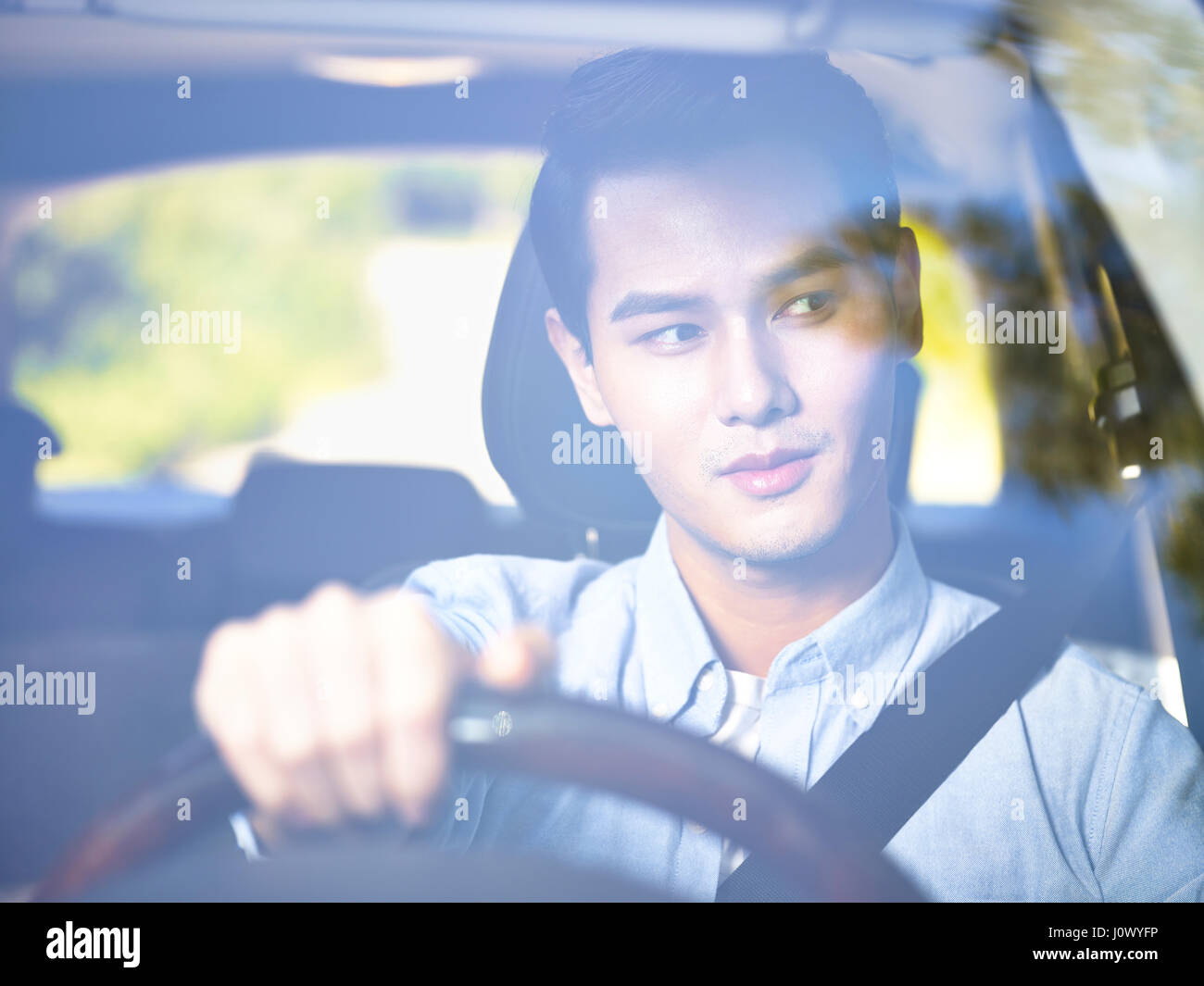 Joven hombre asiático conduciendo un coche vistos a través del parabrisas. Foto de stock