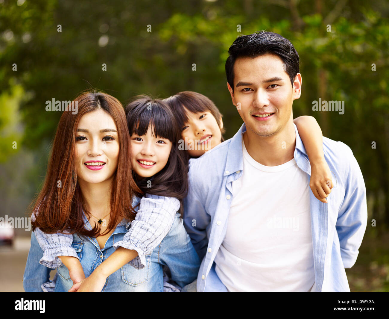 Feliz familia con dos niños asiáticos dando un paseo en el parque arbolado. Foto de stock