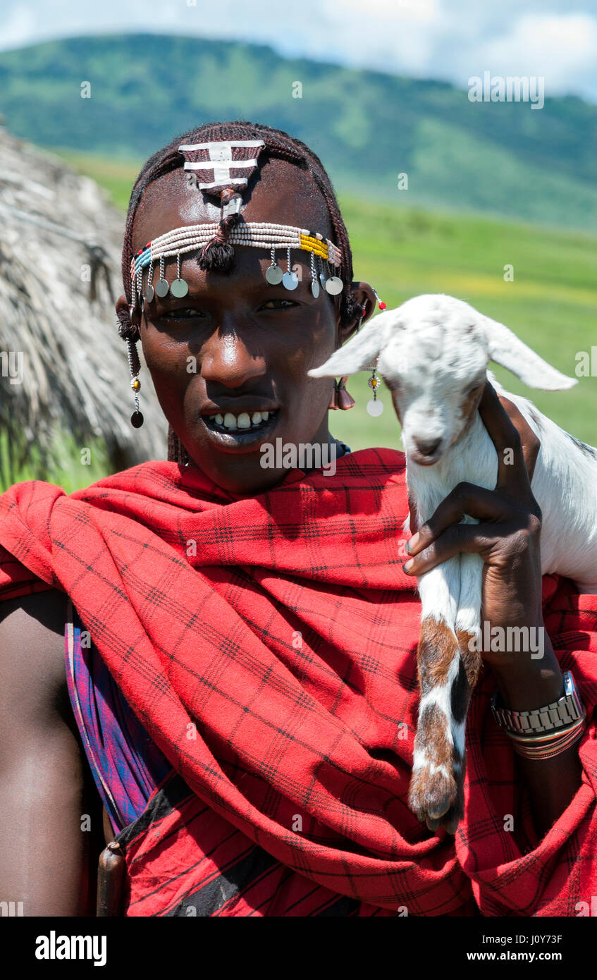 Retrato de un joven guerrero maasai tanzaniano de África oriental en cuentas de joyería tribal y ornamentos de plata, tradicional túnica roja Shuka y Gato Blanco. Foto de stock