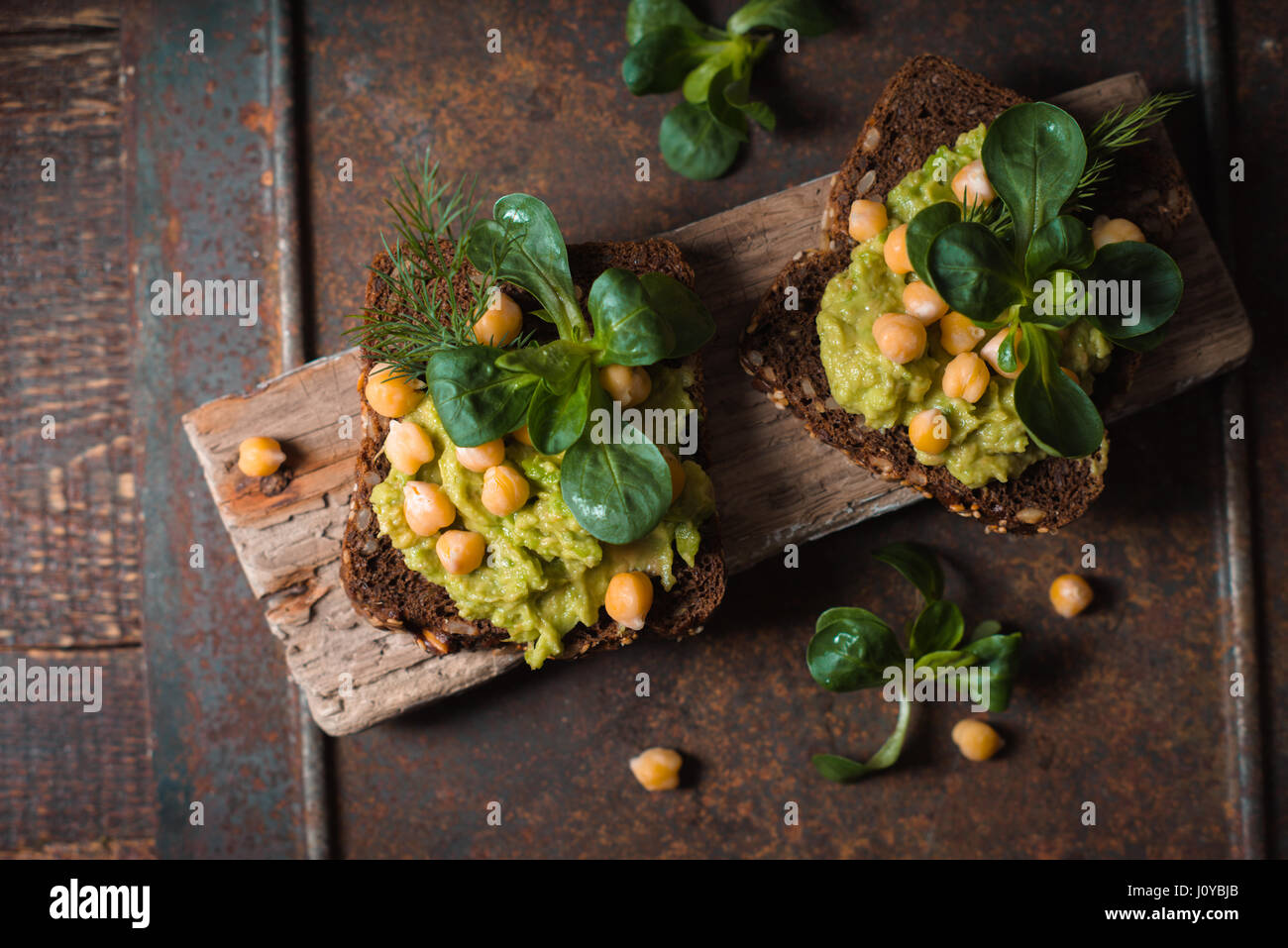 Sándwich abierto con crema de aguacate y verdes en el fondo de metal vista superior Foto de stock