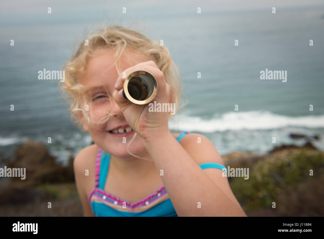 Chica de pie mirando al mar a través de un telescopio Foto de stock