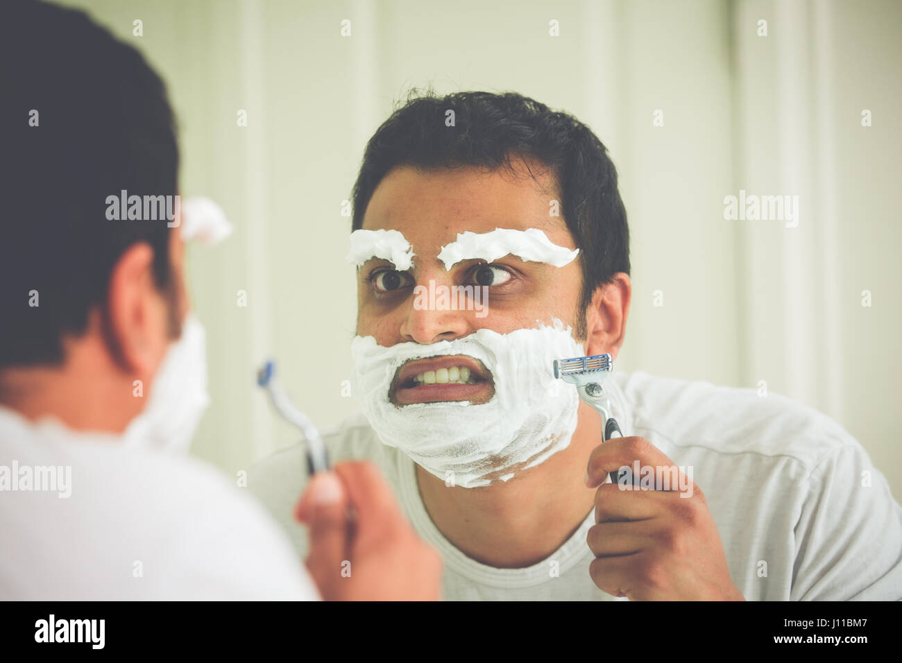 Closeup retrato, puntilloso mentalmente perturbados, Mad Hatter como un hombre joven, al final de su cuerda, intentando afeitarse su rostro cejas y cara, es Foto de stock