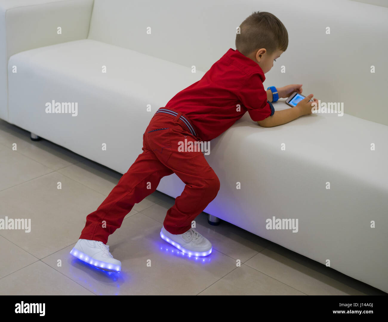 Niño pequeño jugando en el smartphone. Juegos móviles. Él es llevar  zapatillas de LED blanco brillante . Los zapatos con luz Fotografía de  stock - Alamy