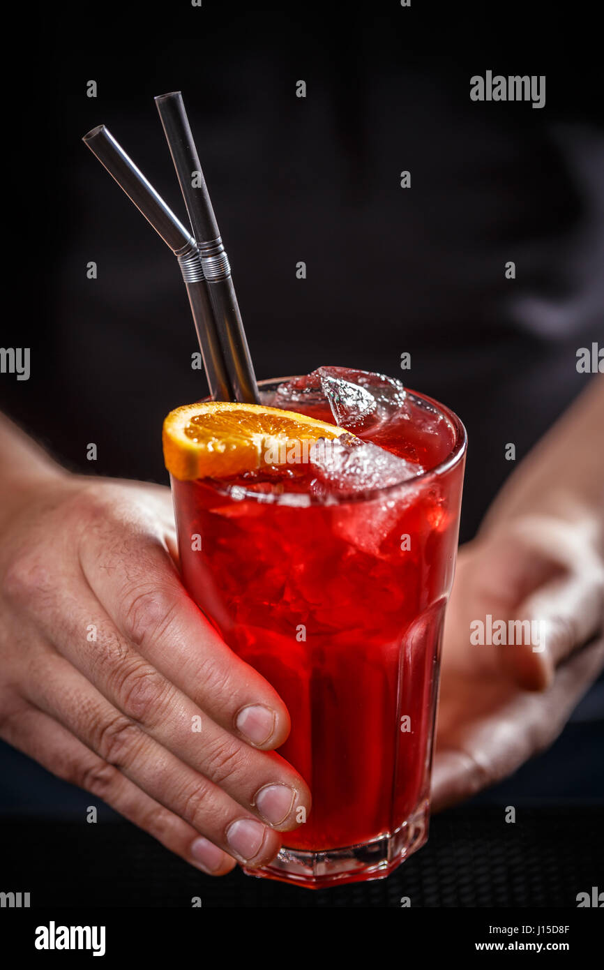 Barman servir rojo cóctel con rodajas de naranja, Ice Cube y paja Foto de stock