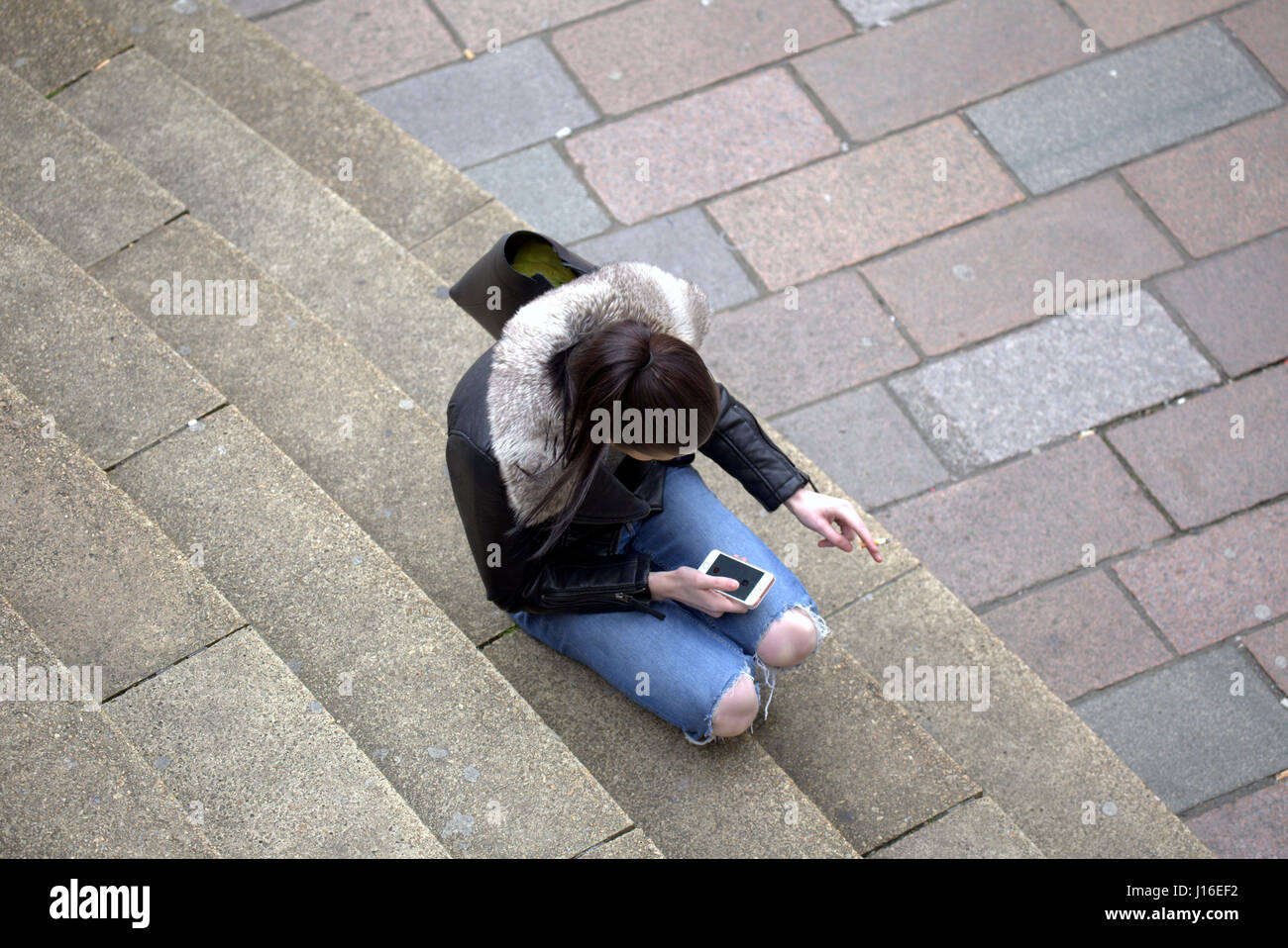 Joven Mujer sentada anf fumar mientras se utiliza el teléfono móvil Glasgow Concert Hall pasos en la confluencia de la calle Buchanan Street Sauchiehall Street Foto de stock