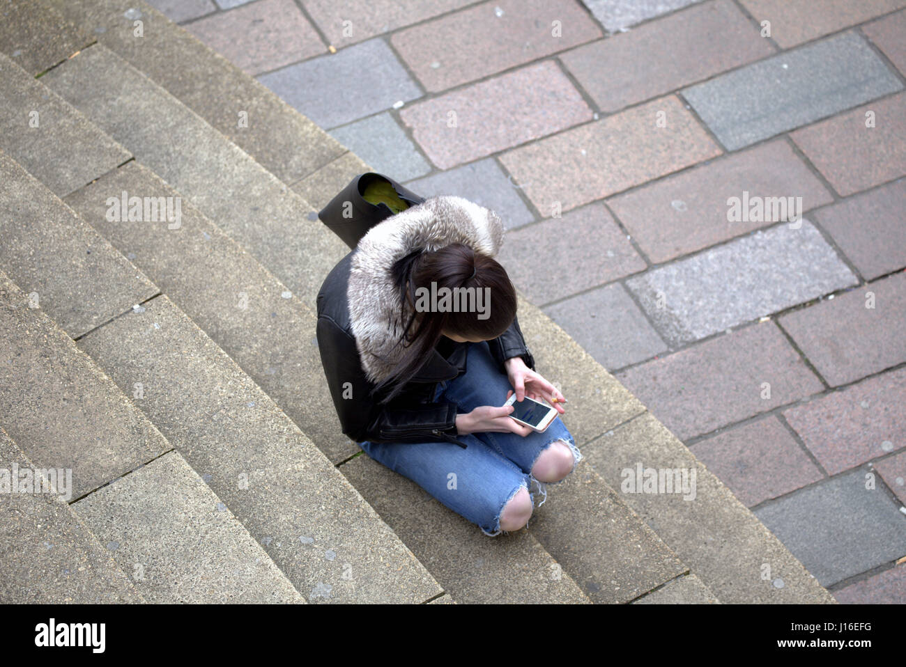 Joven Mujer sentada anf fumar mientras se utiliza el teléfono móvil Glasgow Concert Hall pasos en la confluencia de la calle Buchanan Street Sauchiehall Street Foto de stock