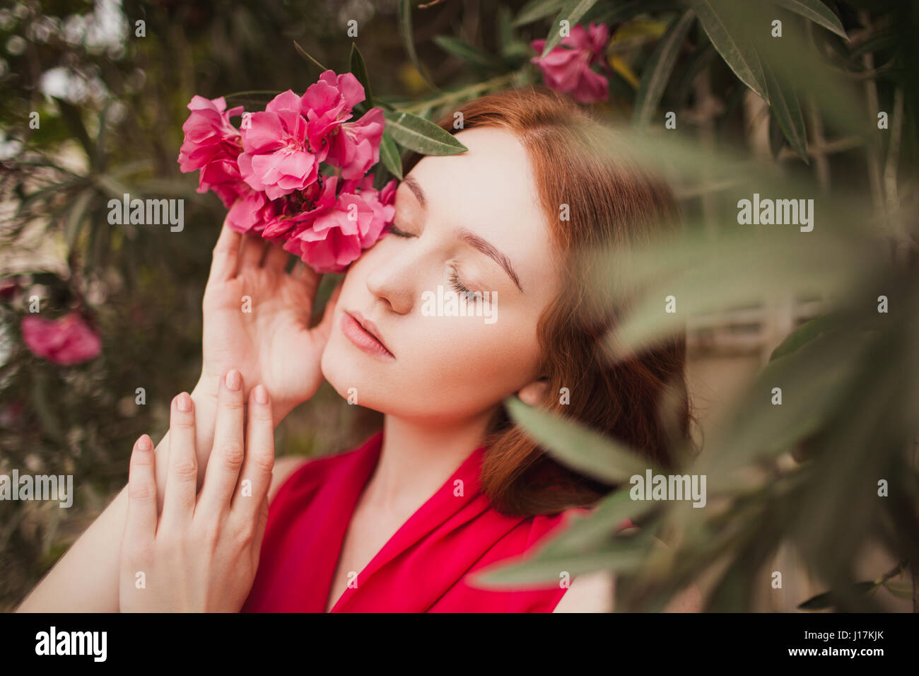 Hermosa chica pelirroja cerró los ojos. En la mano derecha sujetando una flor roja. Retrato Foto de stock