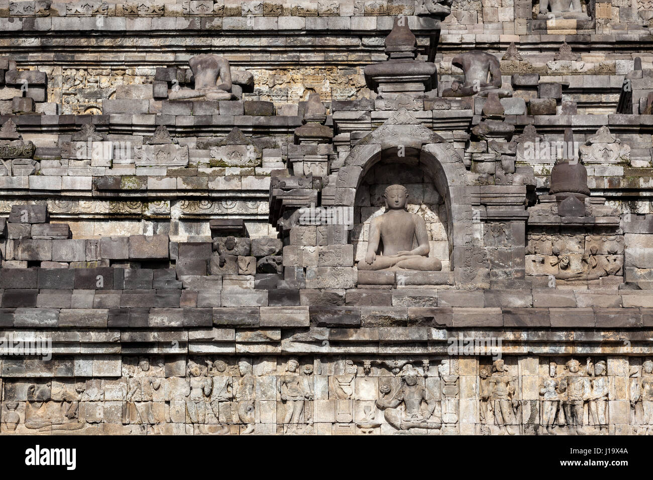 Una estatua de Buda meditando rodeada por relieves en piedra en el Borobudur en Indonesia, en Asia. Foto de stock