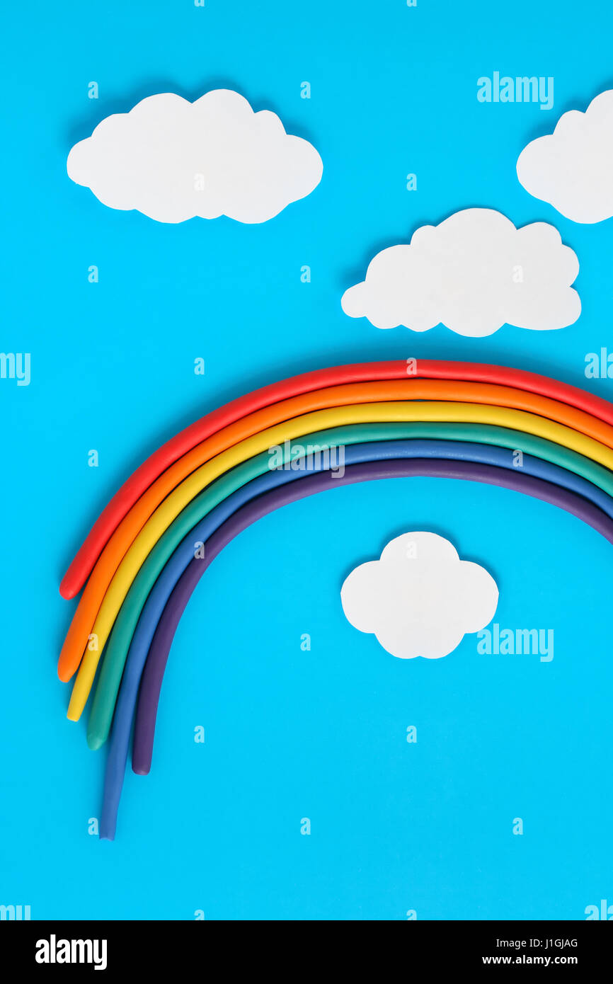 Plastilina rainbow cerca de nubes de papel blanco sobre fondo azul. Foto de stock