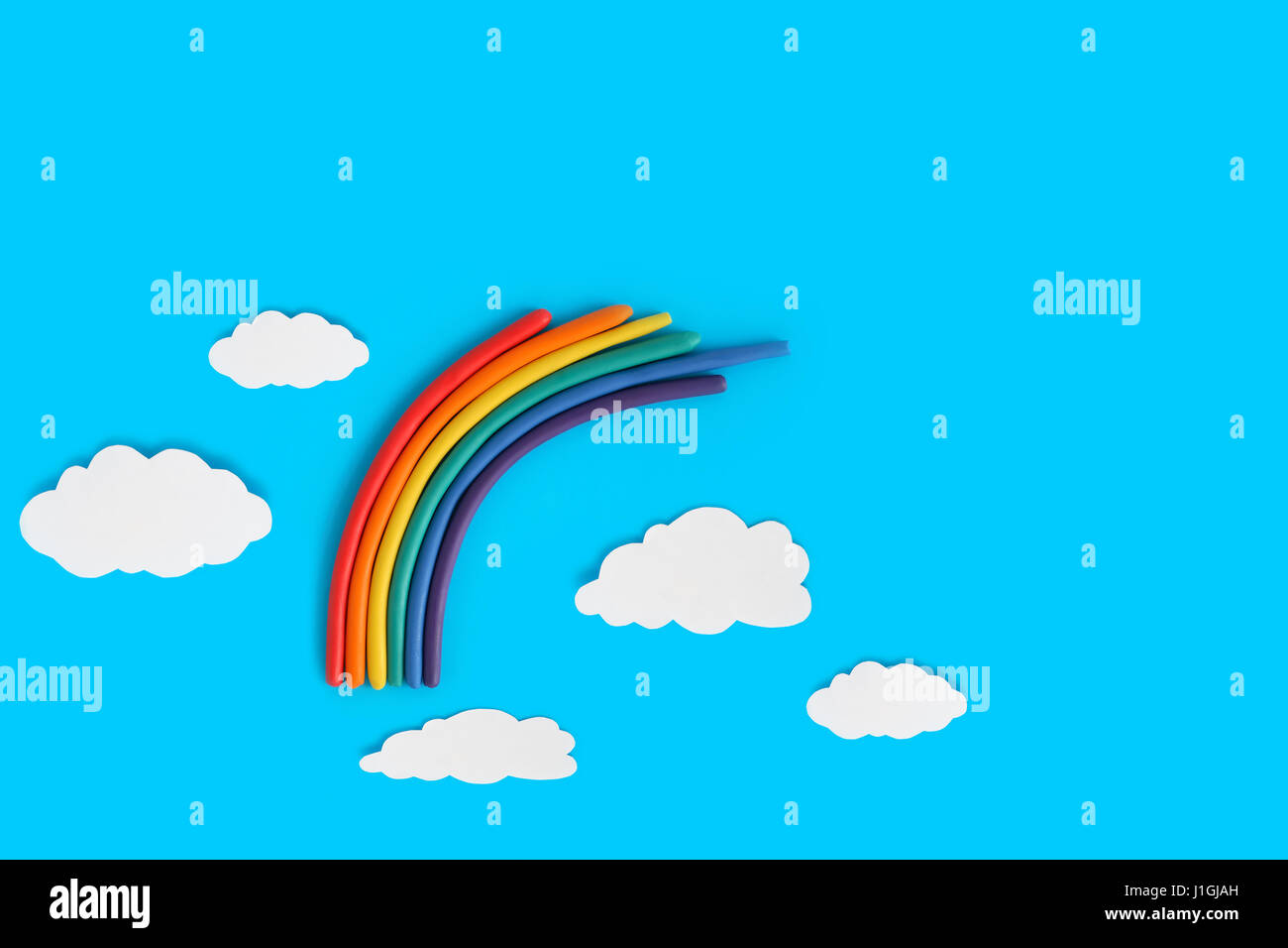 Plastilina rainbow cerca de nubes de papel blanco sobre fondo azul. Foto de stock