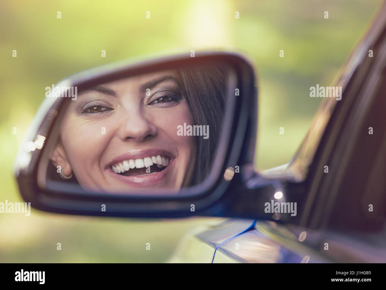 Feliz joven conductor mirando en el espejo retrovisor lateral de coche, asegurándose lane es gratis antes de hacer un giro. Expresión de cara humana positiva las emociones. Seguro Foto de stock