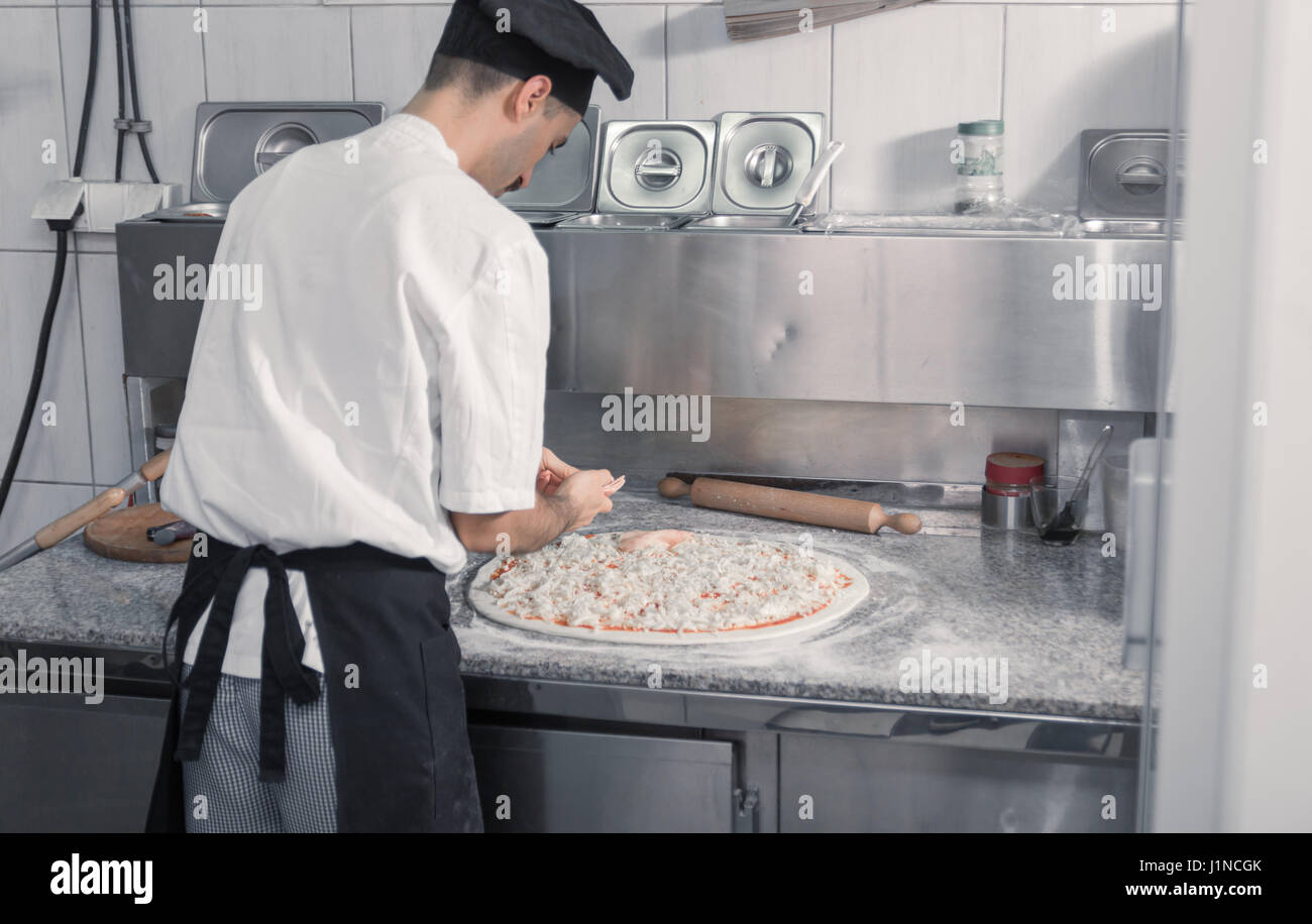 Un hombre adulto profesional joven cocinero haciendo pizzas, cocina comercial Foto de stock