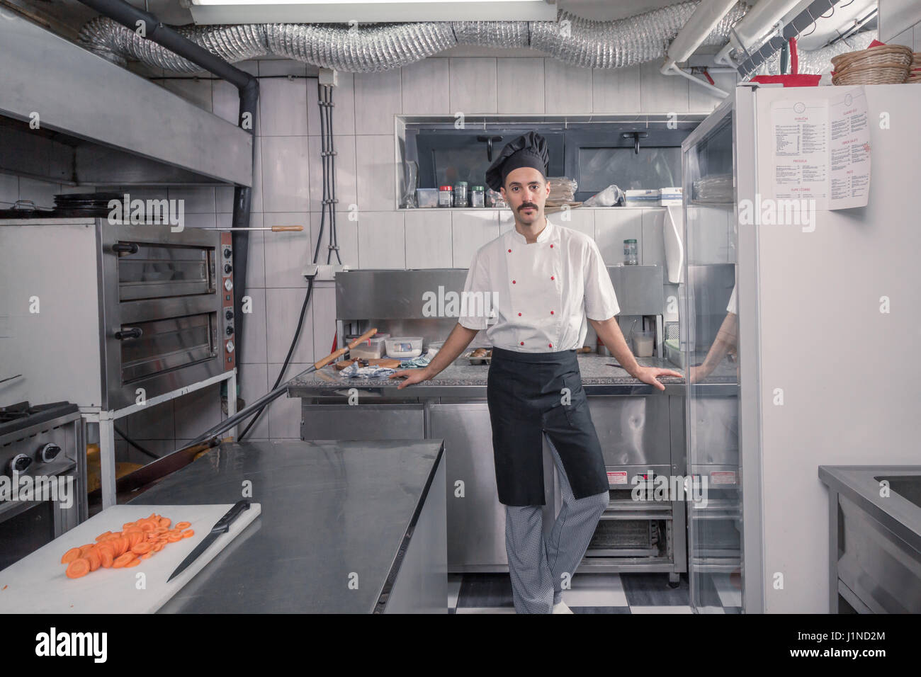 Un hombre adulto, joven chef posando, mirando a la cámara, cocina comercial, profesional Foto de stock