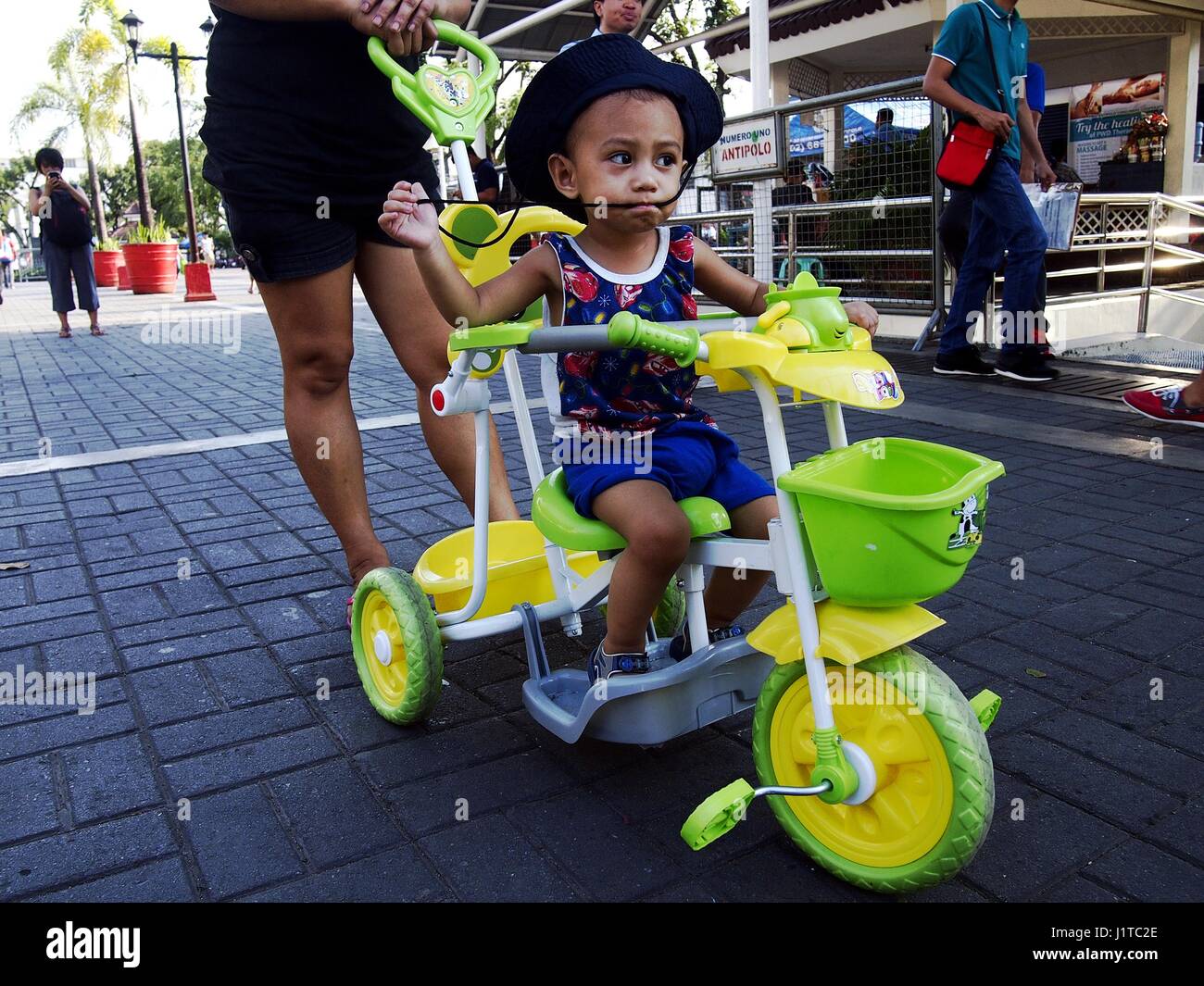 ANTIPOLO CITY, Filipinas - Abril 18, 2017: un joven es empujada por su madre en su colorido kiddie triciclo. Foto de stock
