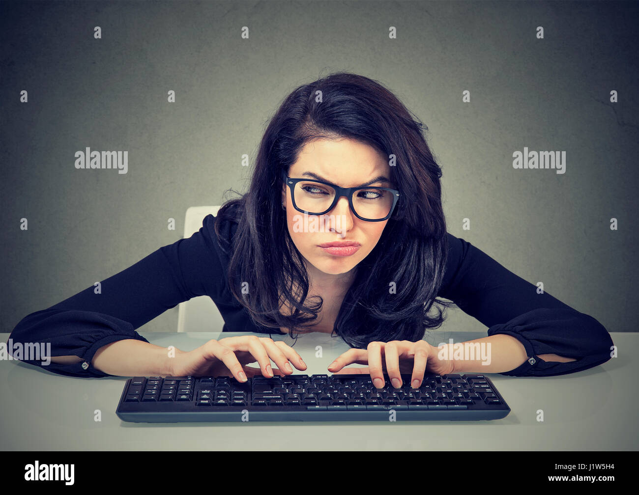Crazy busca mujer nerdy escribiendo en el teclado preguntándose qué responder tramando una venganza Foto de stock