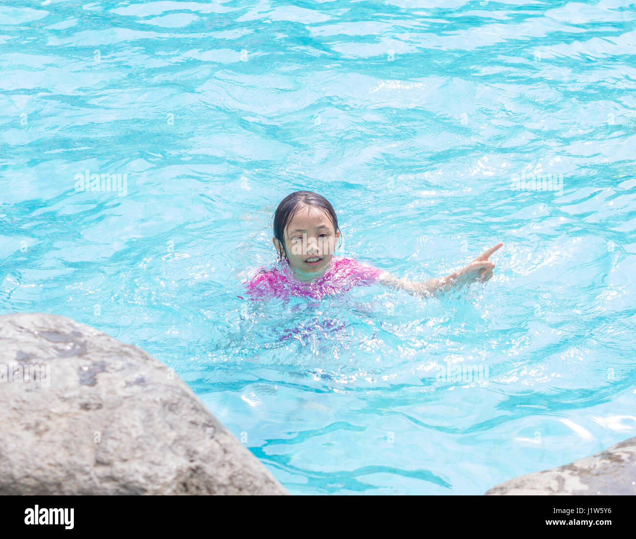 Cabrito asiáticos (niña) en la piscina con finger pointing Foto de stock